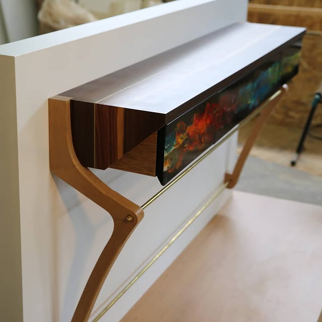 Console suspendue vue de trois quarts, plateau en placage, façades de tiroirs en résine époxy, supports et tringle en laiton