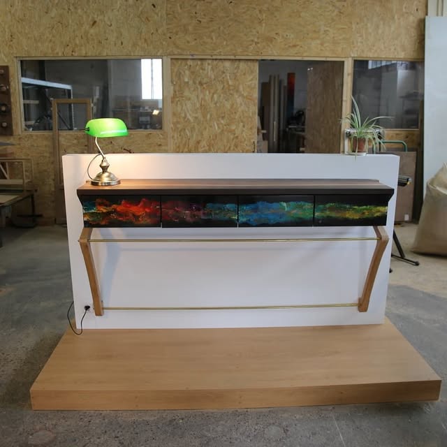 La console suspendue vue de face, fixée sur une cloison blanche à l’atelier, tringle en laiton et supports en bois
