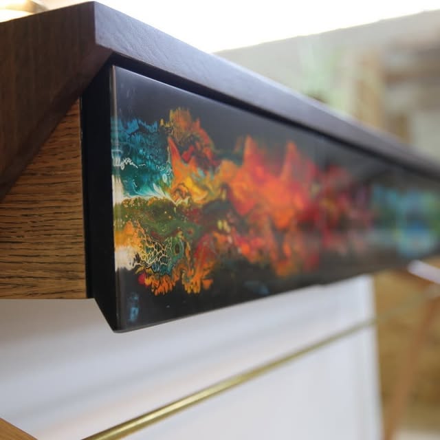 Gros plan sur une coulée de résine époxy orange, verte et bleue prise dans le bois, sous vernis brillant