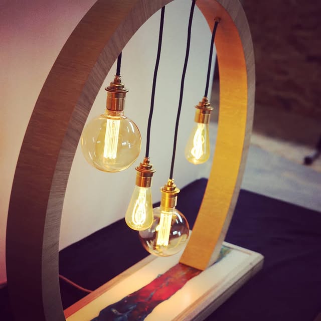 Luminaire en chêne cintré en arche, quatre ampoules à filament suspendues, socle traversé par une coulée de résine bleue et rouge