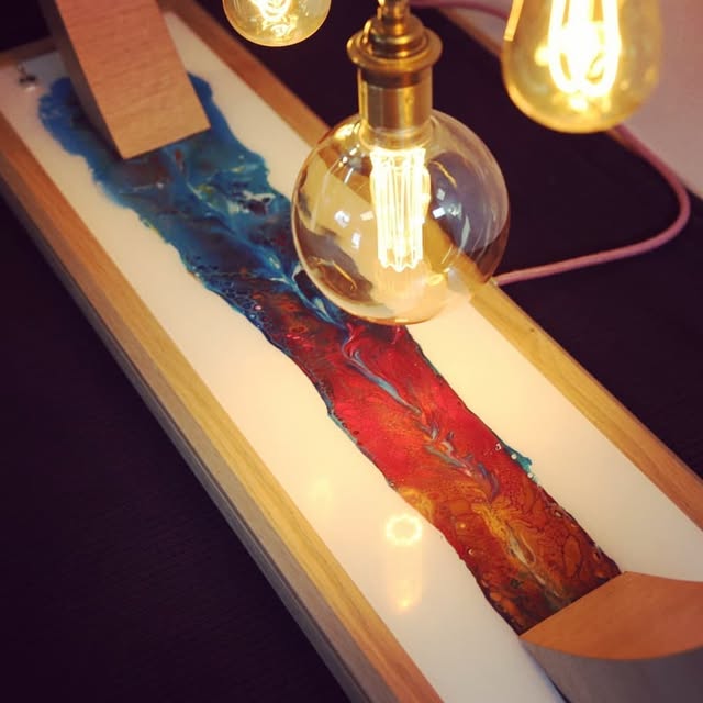 Détail du socle du luminaire : rivière de résine bleue et rouge éclairée par les ampoules à filament